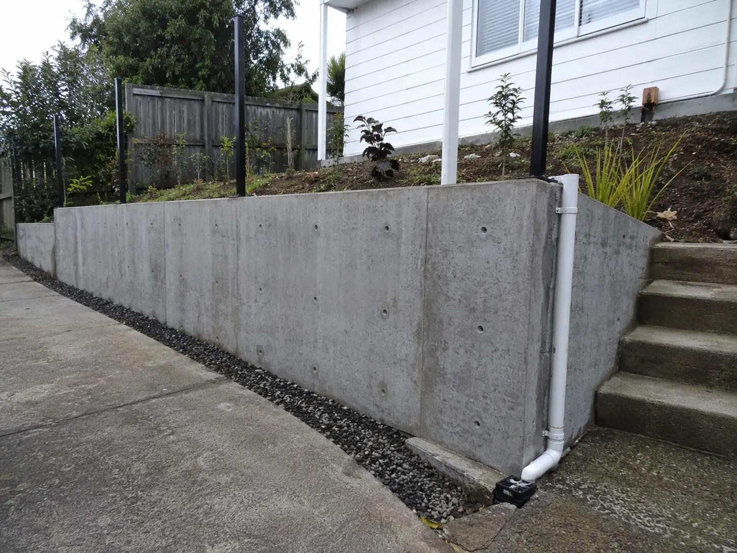 Poured concrete retaining wall with a drainage channel along its footing